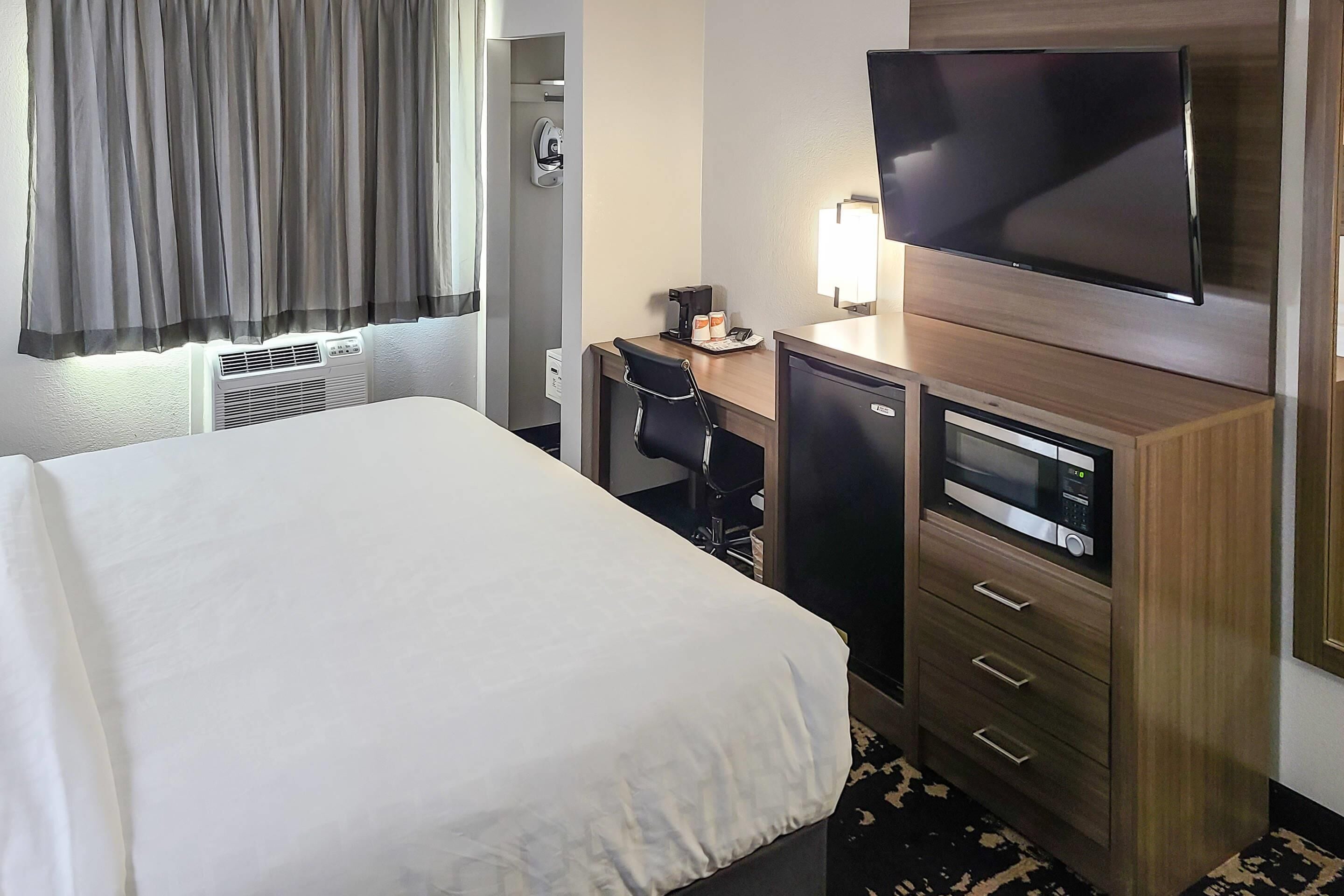 A hotel room with a bed, a desk with a chair, a television, and a microwave.