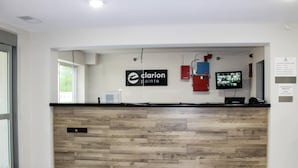 A reception desk with a wooden panel design, a mounted television, and a red fire extinguisher. - Clarion Pointe Bettendorf - Quad Cities (Bettendorf)
