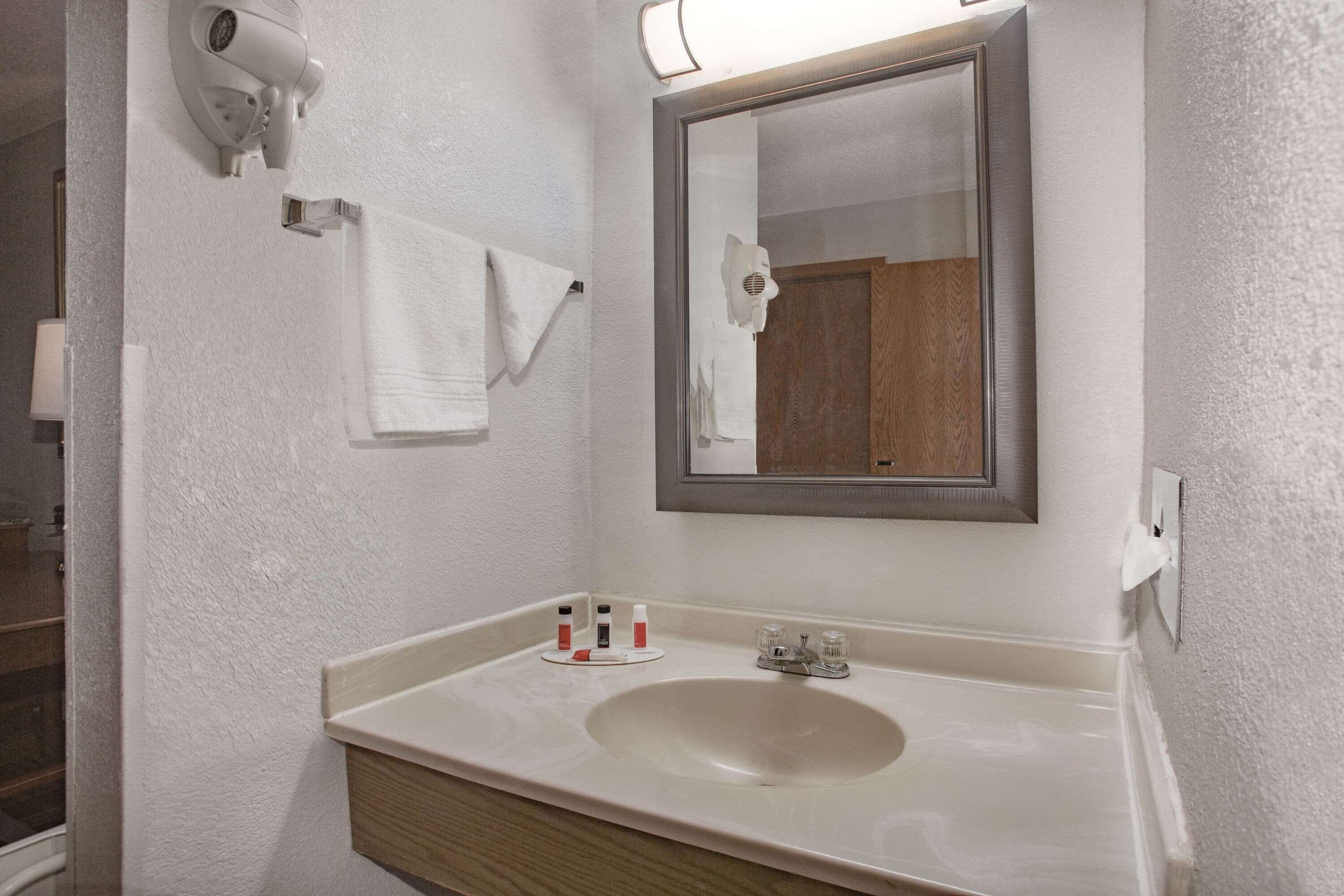 Un baño con lavamanos, espejo, toallero y secador de pelo.