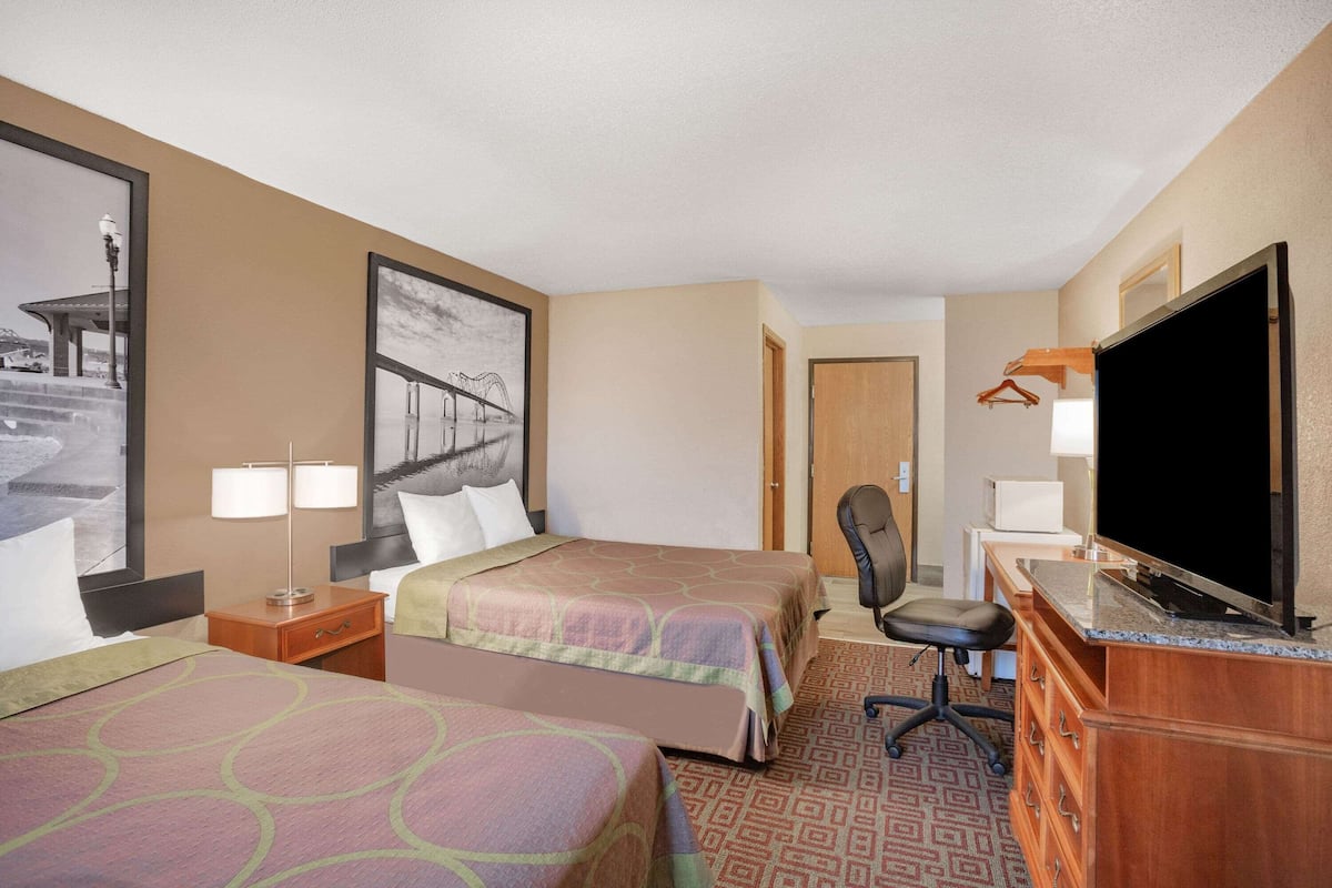 Une chambre d’hôtel avec deux lits, un bureau avec une télévision, une chaise et une commode.