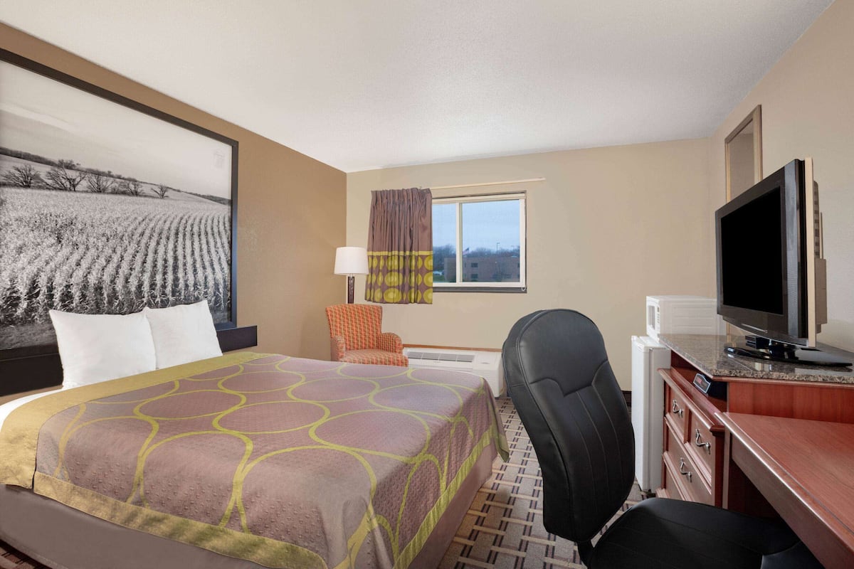 Une chambre d’hôtel avec un lit, un bureau avec une télévision, une chaise et une fenêtre avec des rideaux.