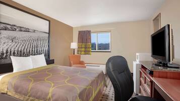 A hotel room with a bed, a desk with a television, a chair, and a window with curtains.