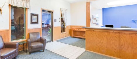 A reception area with a wooden desk, two leather chairs, a tiled floor, and a blue wall.
