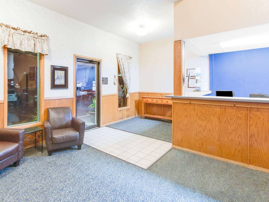 Un área de recepción con un escritorio de madera, dos sillones de cuero, piso de baldosas y pared azul.