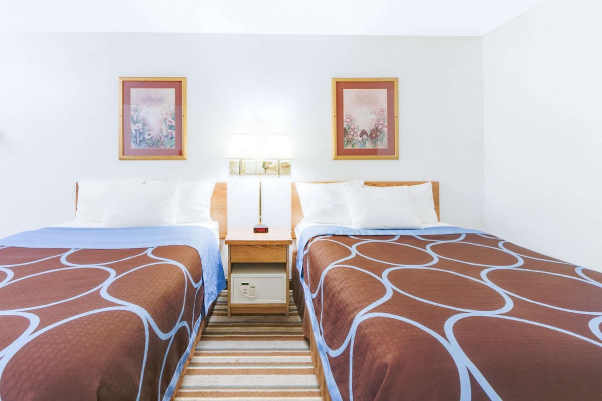 Ein Hotelzimmer mit zwei Betten, einem Nachttisch mit Lampe und zwei gerahmten floralen Bildern an der Wand.