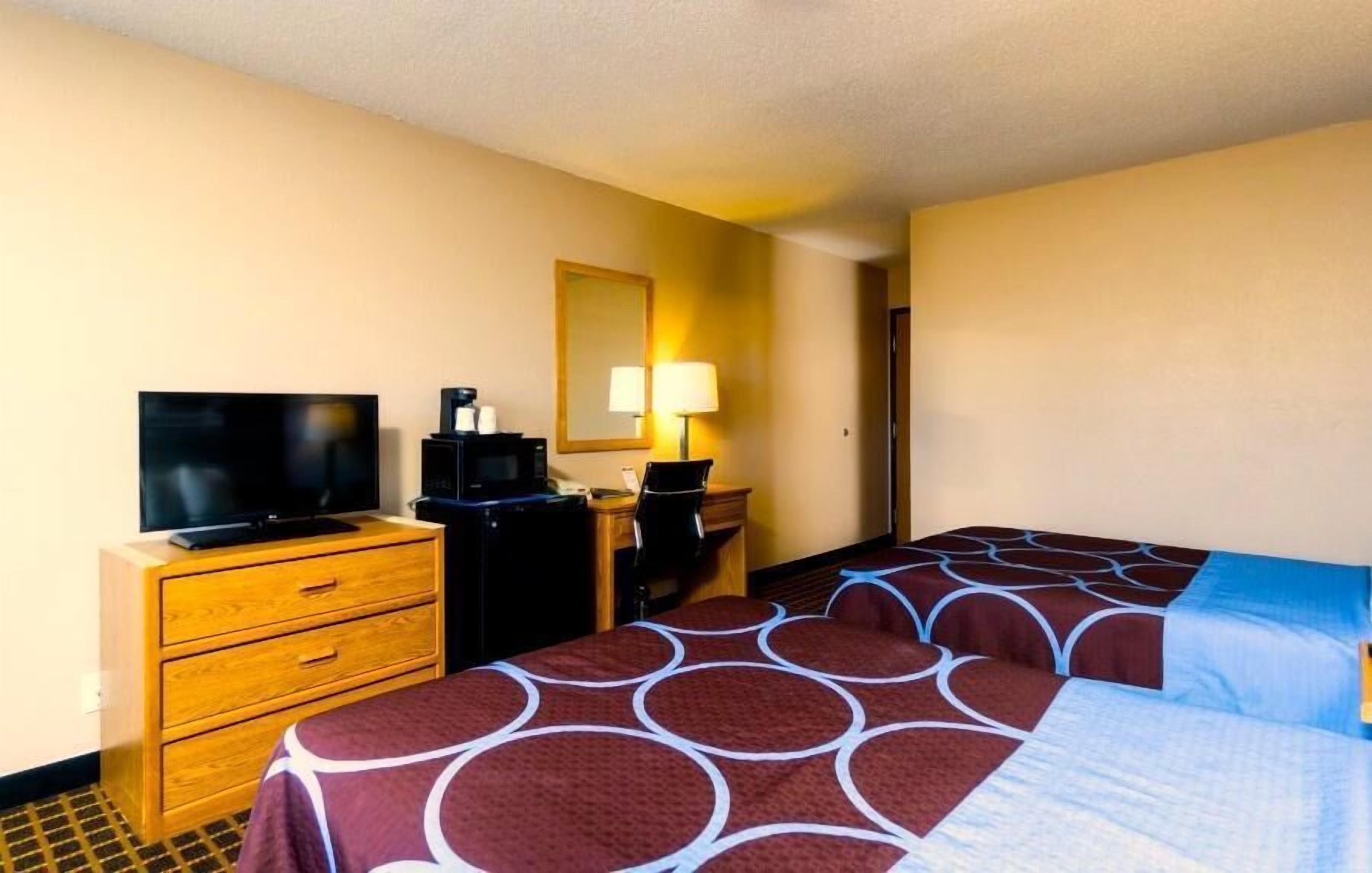 A hotel room with a TV, desk, chair, and two beds with patterned bedspreads.