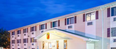 Un motel con una hilera de habitaciones, un acceso cubierto y un letrero que muestra el nombre y número del establecimiento.