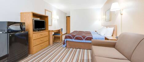 A hotel room with a bed, a sofa, a desk with a computer, a microwave, and a refrigerator.