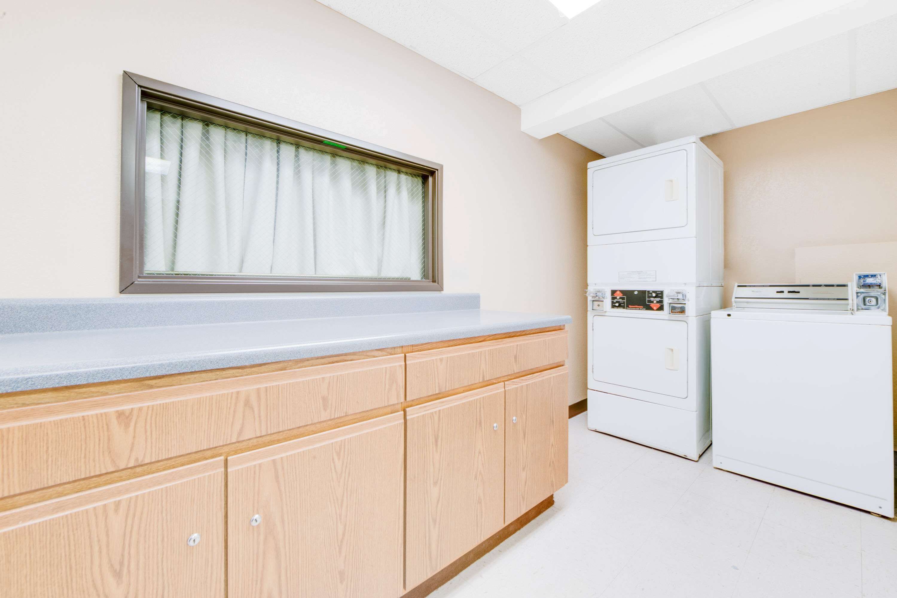 A laundry room with wooden cabinets, a window with curtains, and two stacked washing machines.