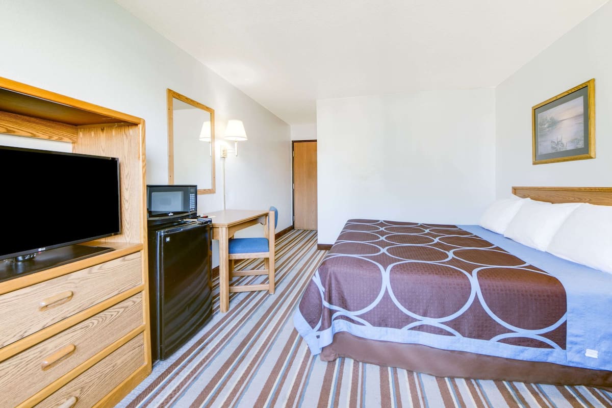 Ein Hotelzimmer mit einem Bett, einem Schreibtisch mit Computer, einem Fernseher und einem Kühlschrank.