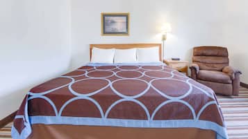 A hotel room with a bed, a chair, a nightstand, a lamp, and a framed picture on the wall.