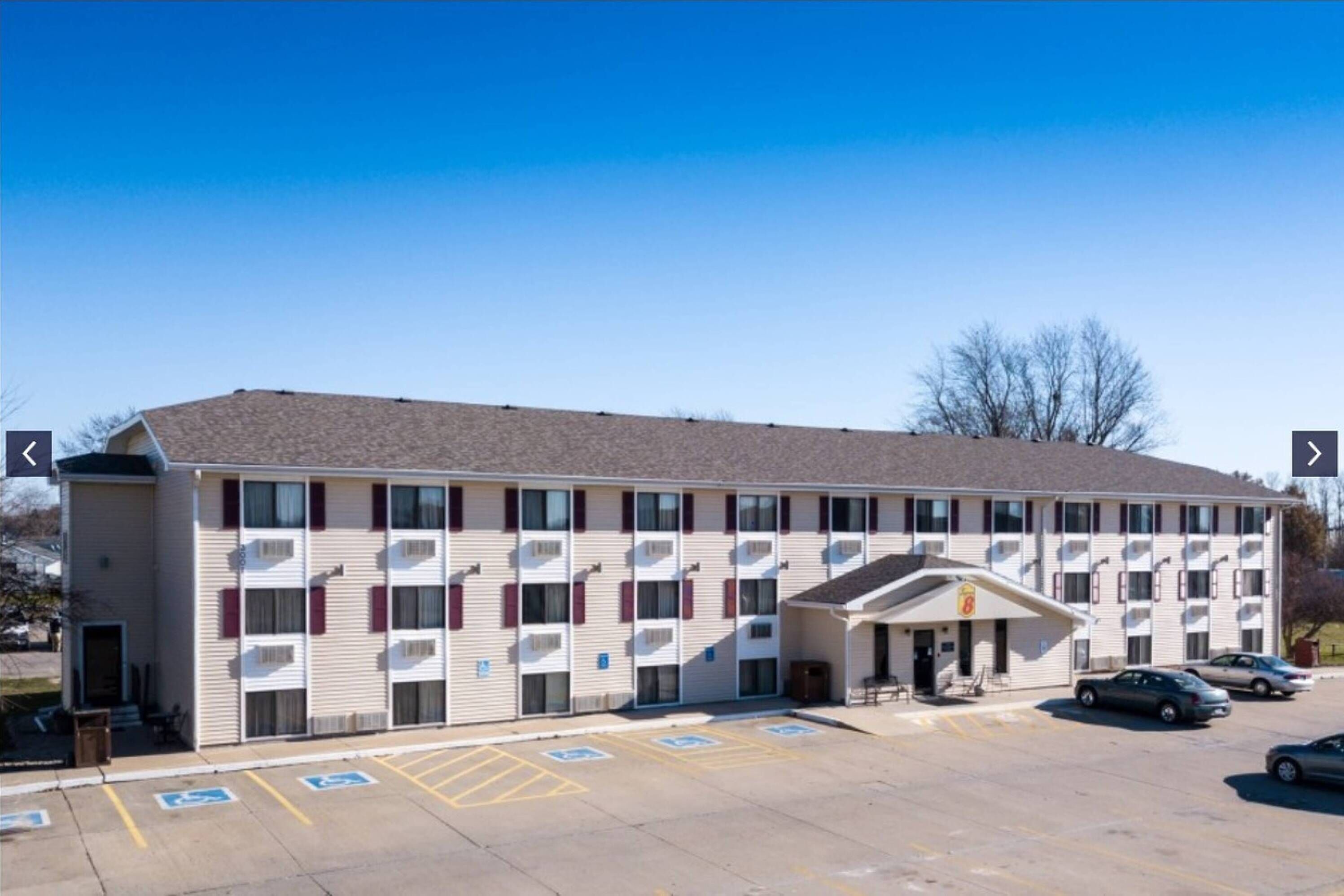 A motel with a central entrance, multiple parking spaces, and a clear sky.