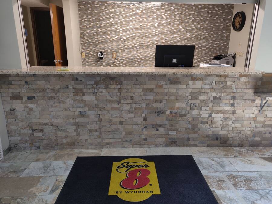 Un área de recepción con una pared de mosaicos, un mostrador de recepción y un tapete con el logotipo en el suelo.