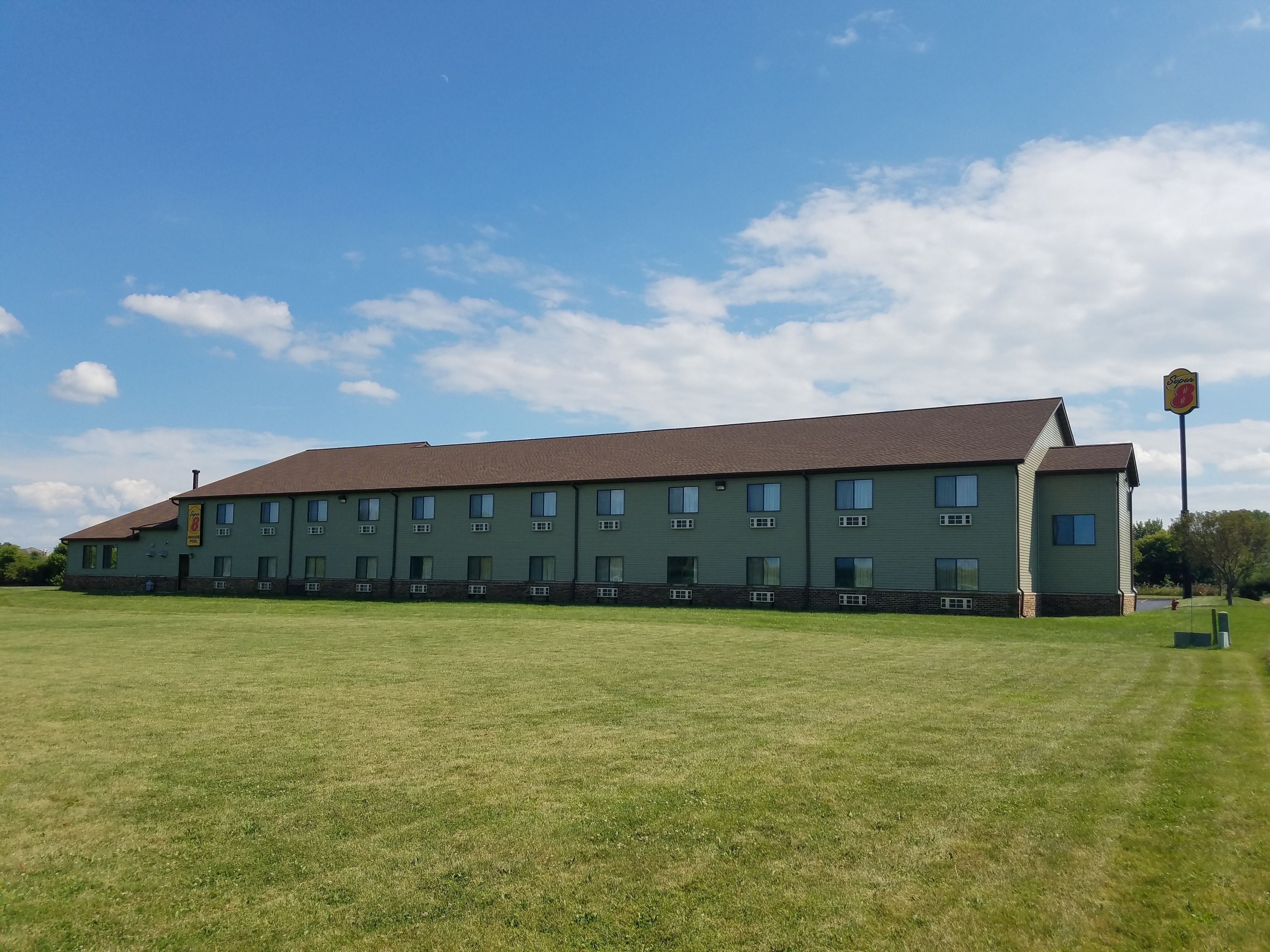 A large, single-story building with a flat roof and multiple windows, surrounded by a grassy field.