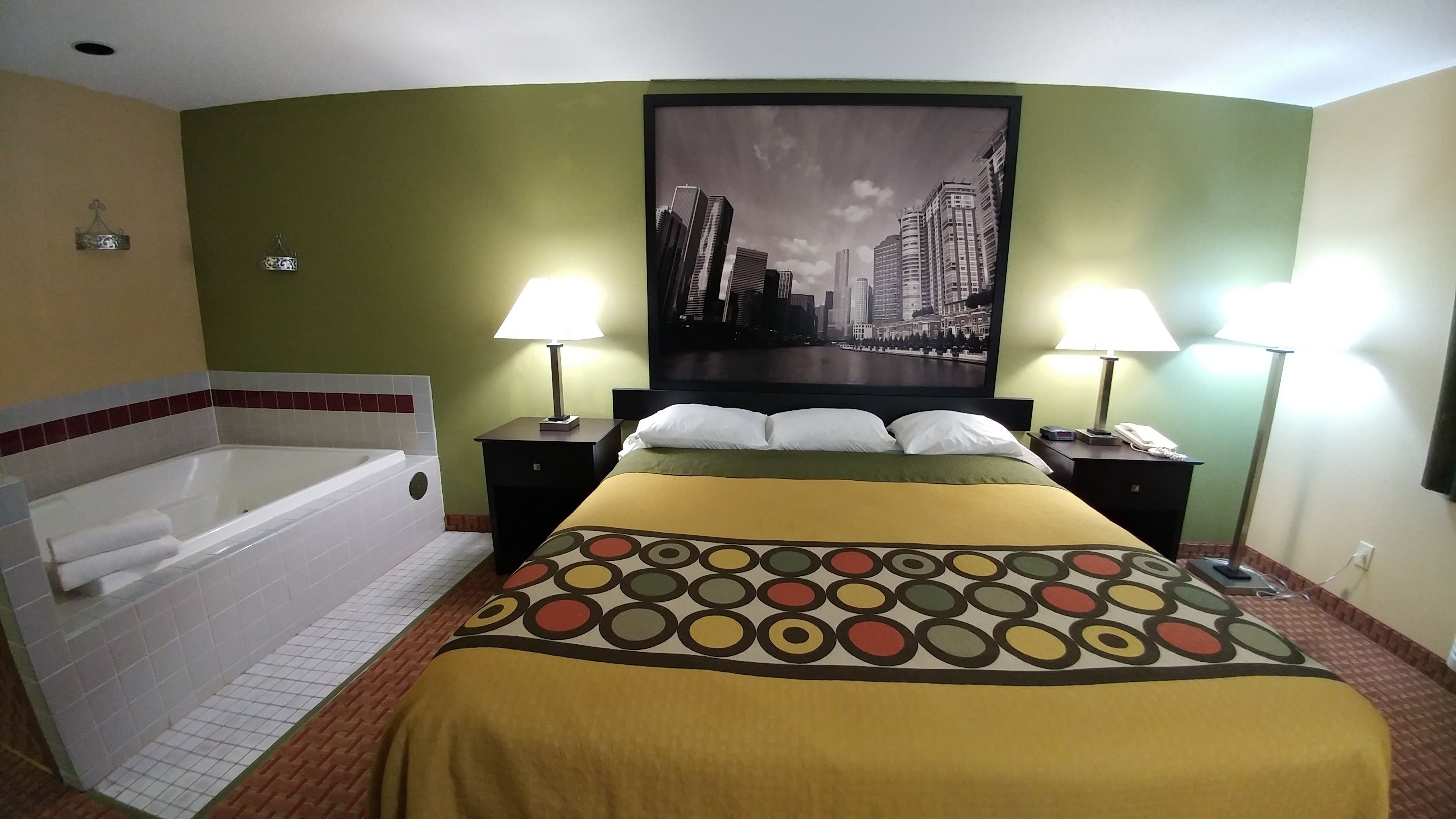 Un cuarto de hotel con una cama grande, dos lámparas de noche, un mesita de noche, un teléfono en la pared y un ventanal con vista a la ciudad.
