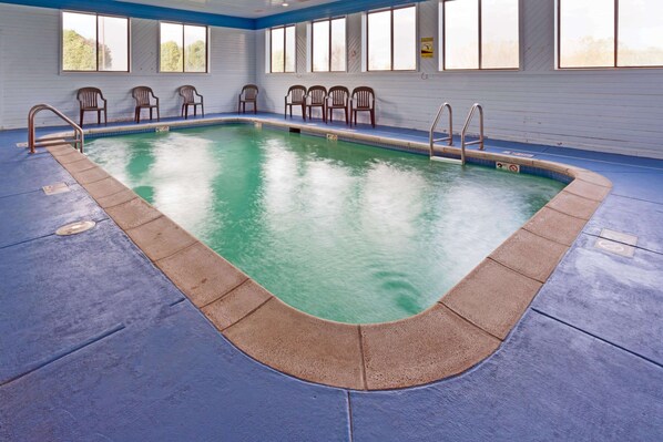 Una piscina interior con agua cristalina, rodeada de suelo azul y sillas de madera.
