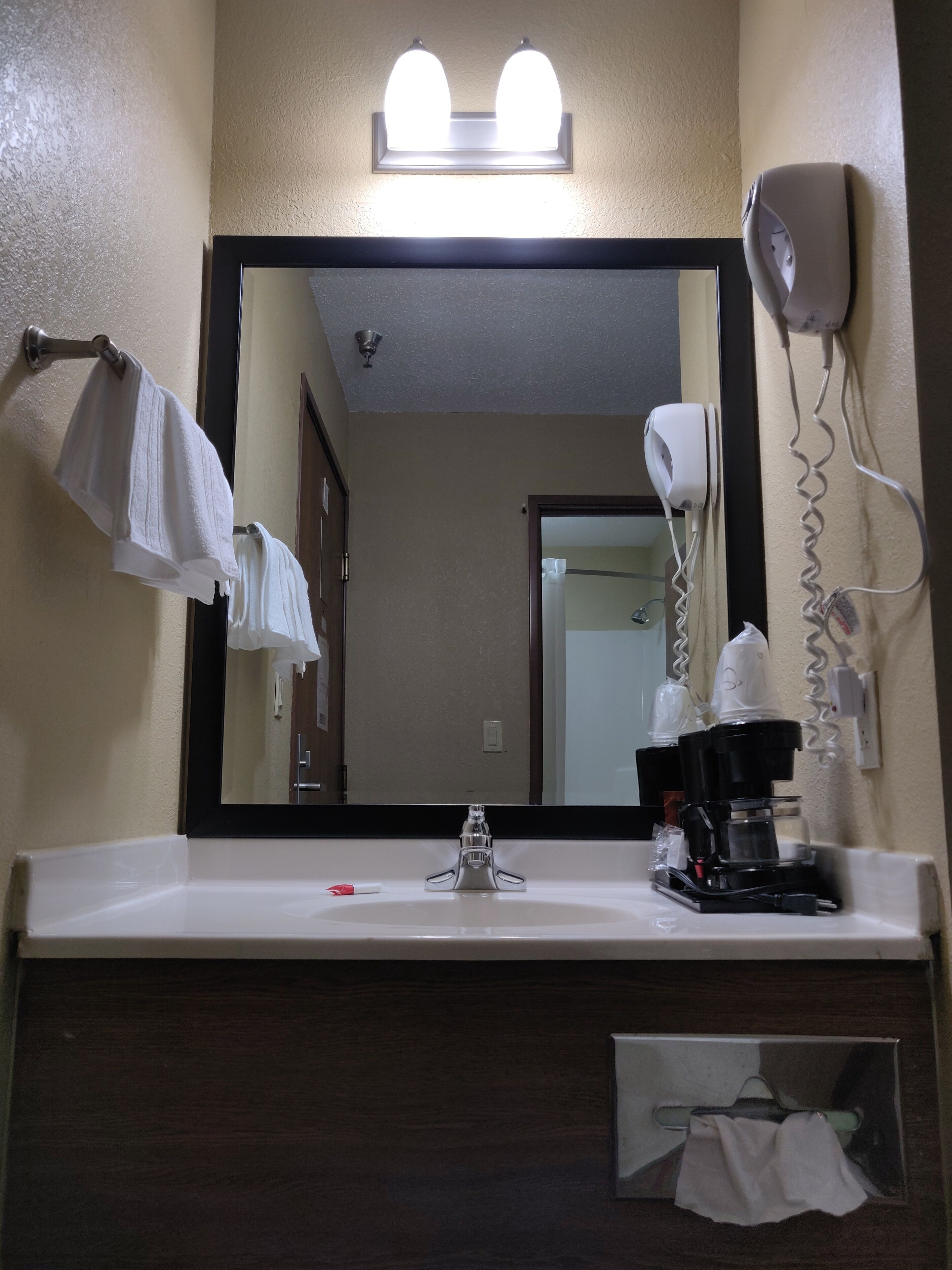 A hotel bathroom with a sink, mirror, towel rack, hair dryer, and coffee maker.