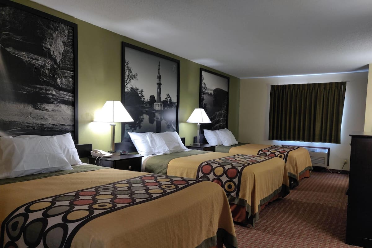 Een hotelkamer met drie bedden, elk met een beddekleed met een patroon, een bureau met een lamp en een groot, ingelijst schilderij aan de muur.