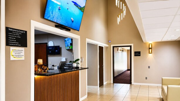 A hotel reception area with a reception desk, a television mounted above it, and a hallway leading to other rooms. - Super 8 by Wyndham Champaign (Champaign)