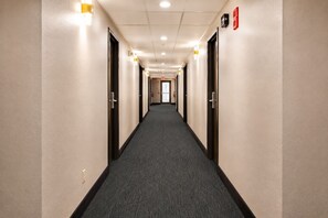 A hotel hallway with carpeted floors, doors on both sides, and recessed lighting. - Super 8 by Wyndham Champaign (Champaign)