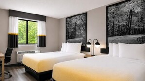 A hotel room with two beds, a desk, a chair, an air conditioning unit, and two wall-mounted lamps. - Super 8 by Wyndham Champaign (Champaign)