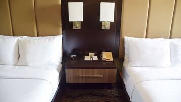 A hotel room with two beds, a nightstand with a lamp, a clock, a telephone, and a small drawer.