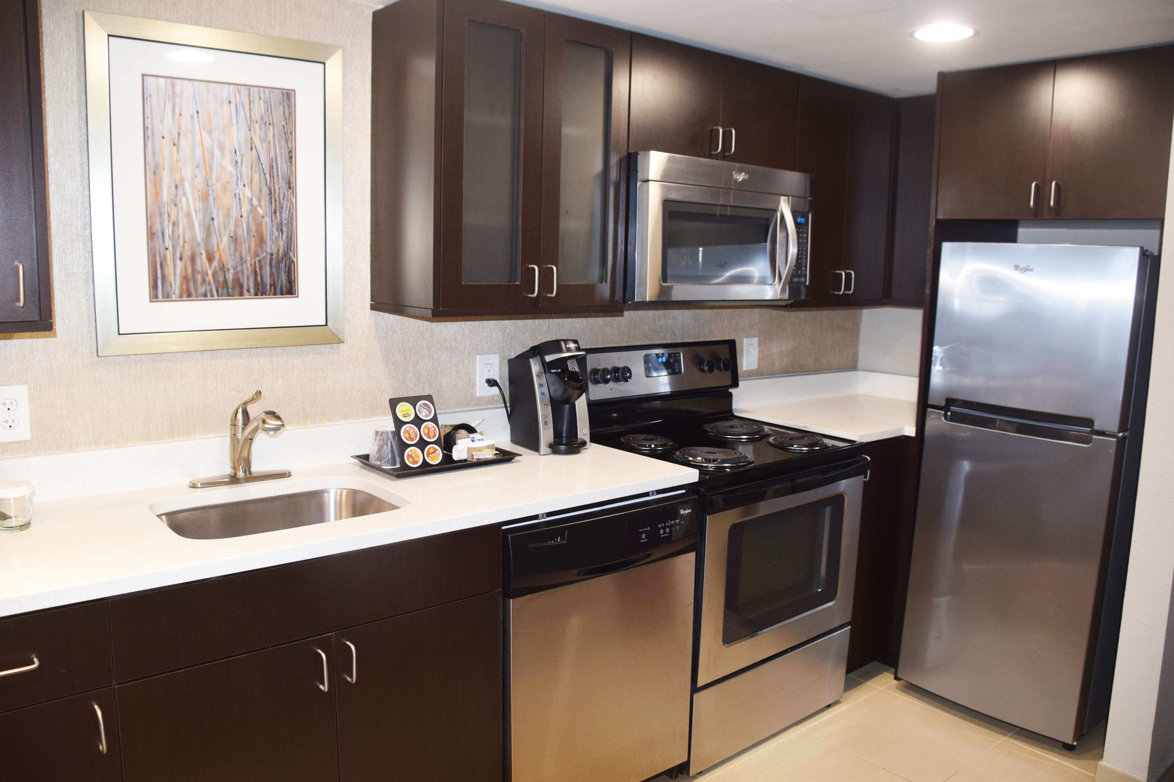 A modern kitchen with dark wooden cabinets, stainless steel appliances including a refrigerator, oven, and microwave, and a dishwasher.