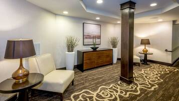 A lobby with a sofa, a table with a lamp, a wooden cabinet, and a patterned carpet.