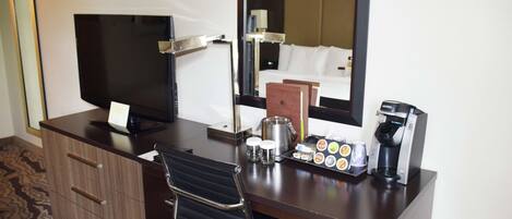 Une chambre d’hôtel équipée d’un bureau, d’une télévision à écran plat, d’une machine à café, d’un miroir et d’un lit avec du linge de lit blanc.