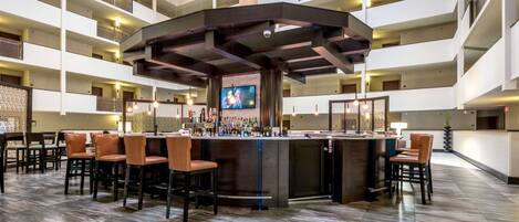 A spacious lobby with a central bar area, multiple seating arrangements, and a high ceiling with exposed structural beams.