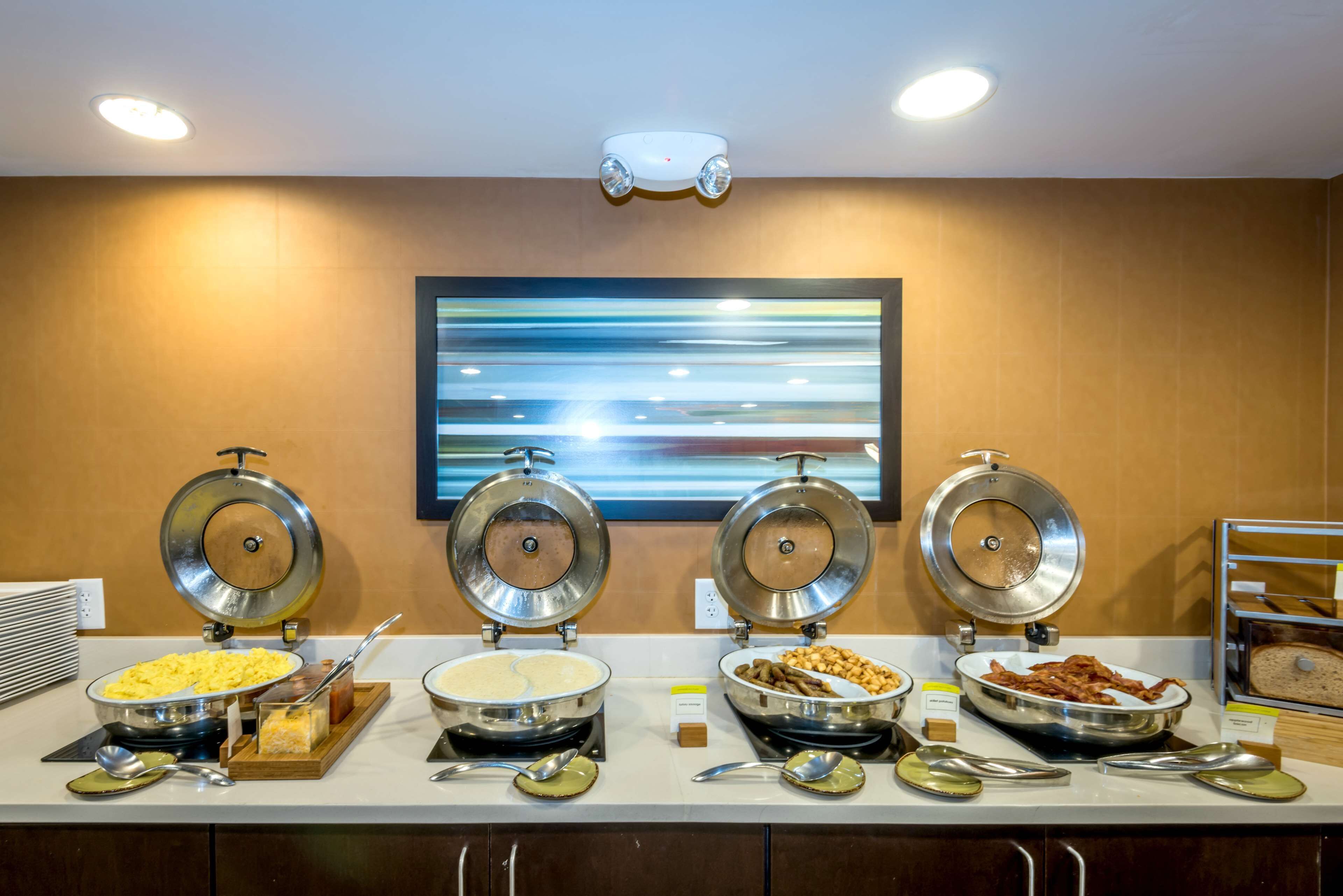 A buffet with various food items, including eggs, cereal, nuts, and bacon, arranged on a counter with a modern design and a large abstract painting on the wall.