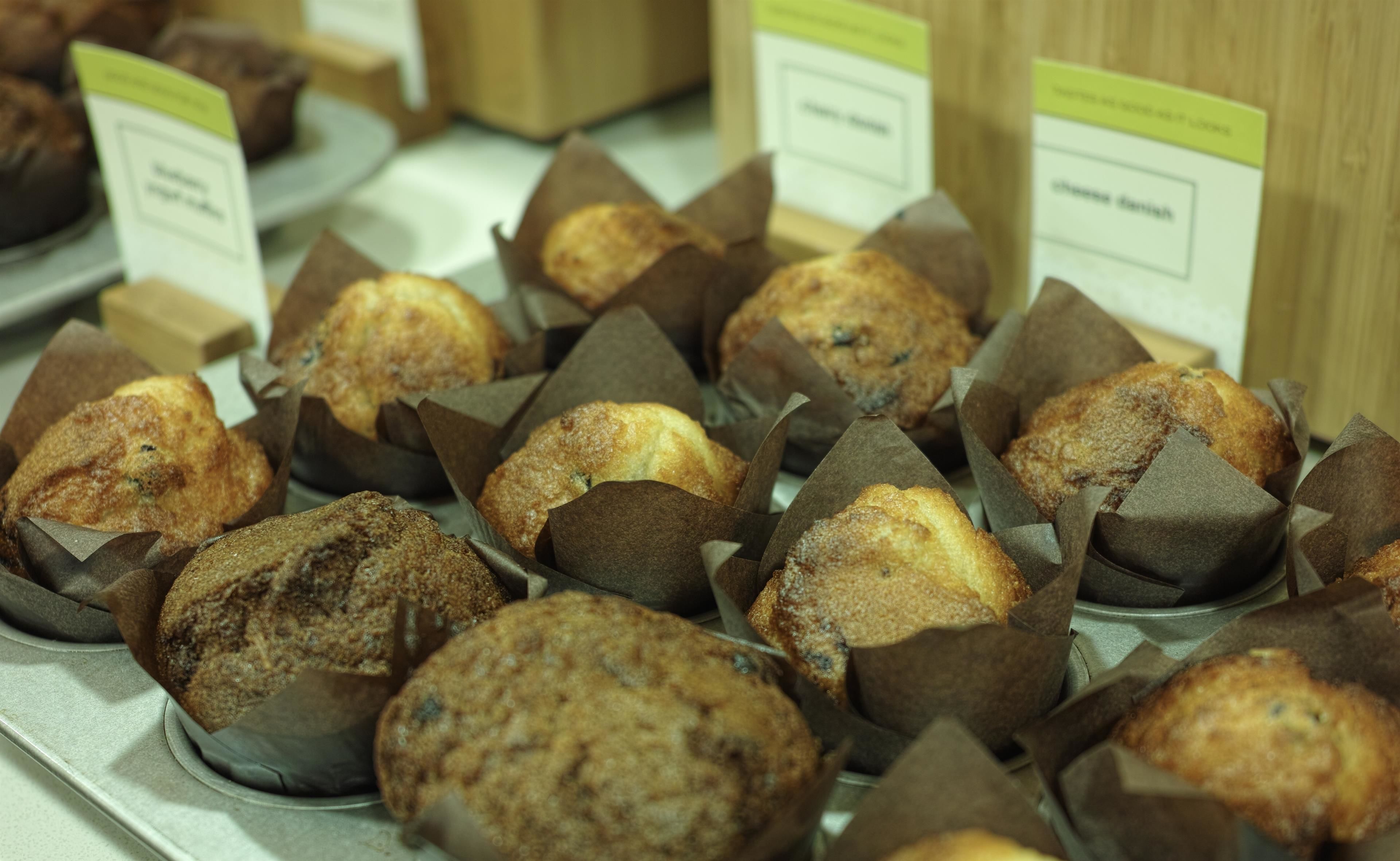 A display of muffins in paper cups with labels.