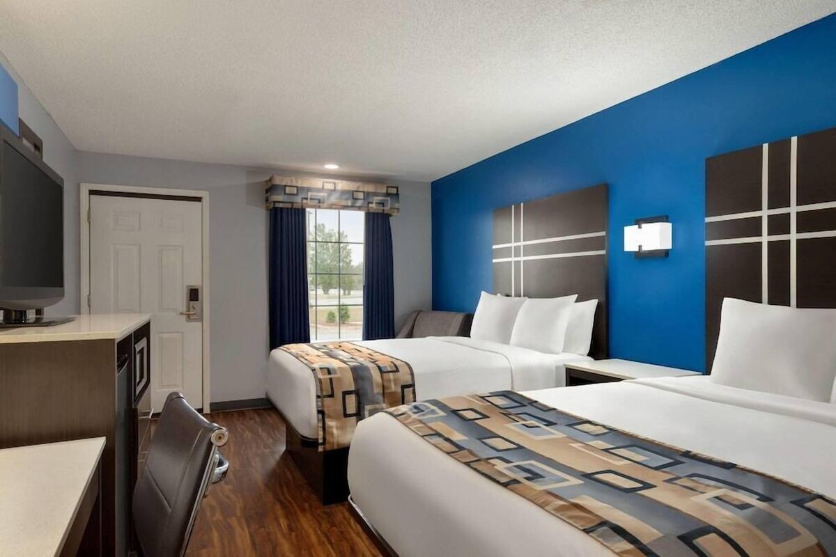 A hotel room with two beds, a desk, a television, and a window with curtains.
