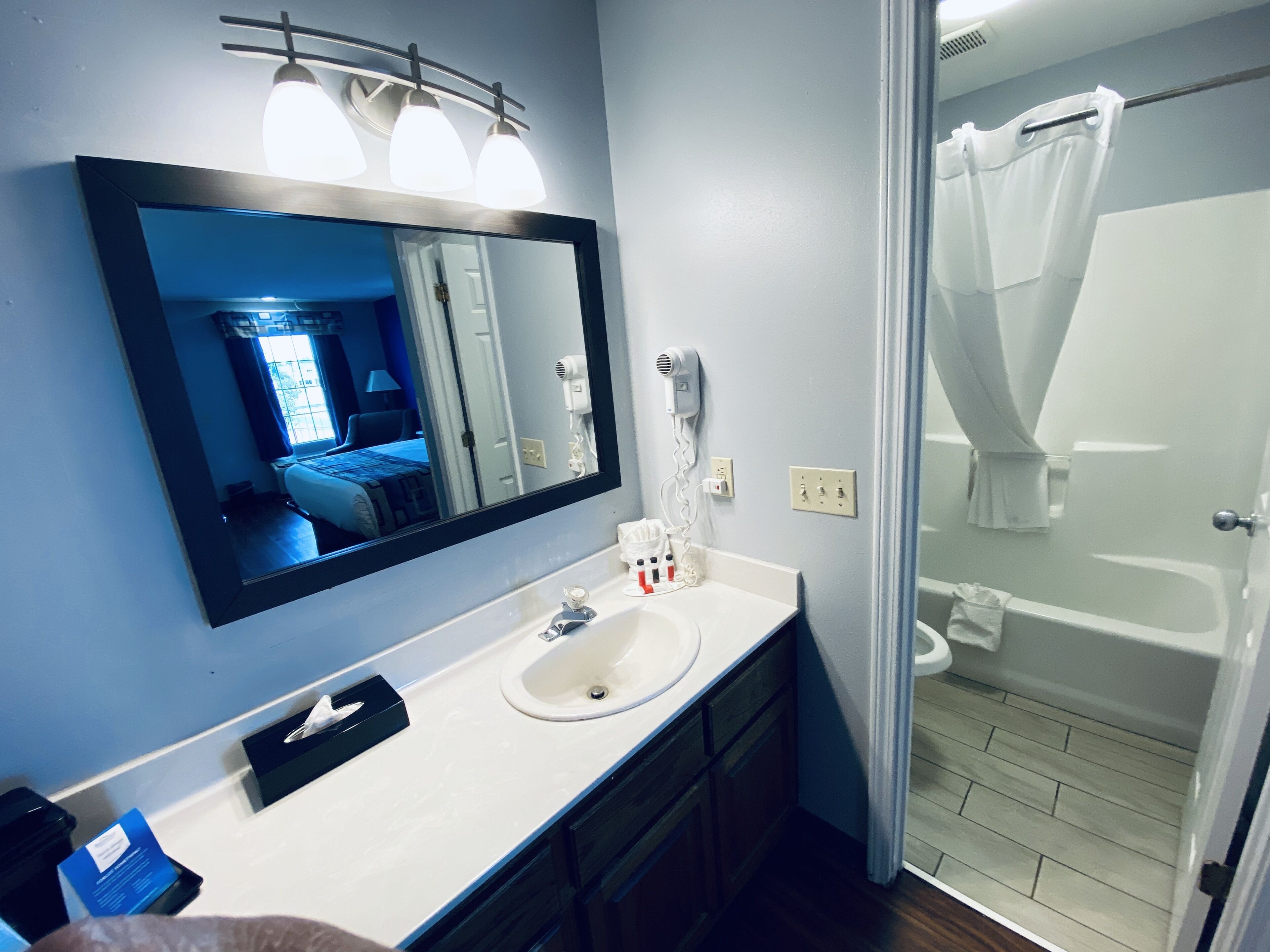 A bathroom with a large mirror, a sink, a hairdryer, and a shower curtain.