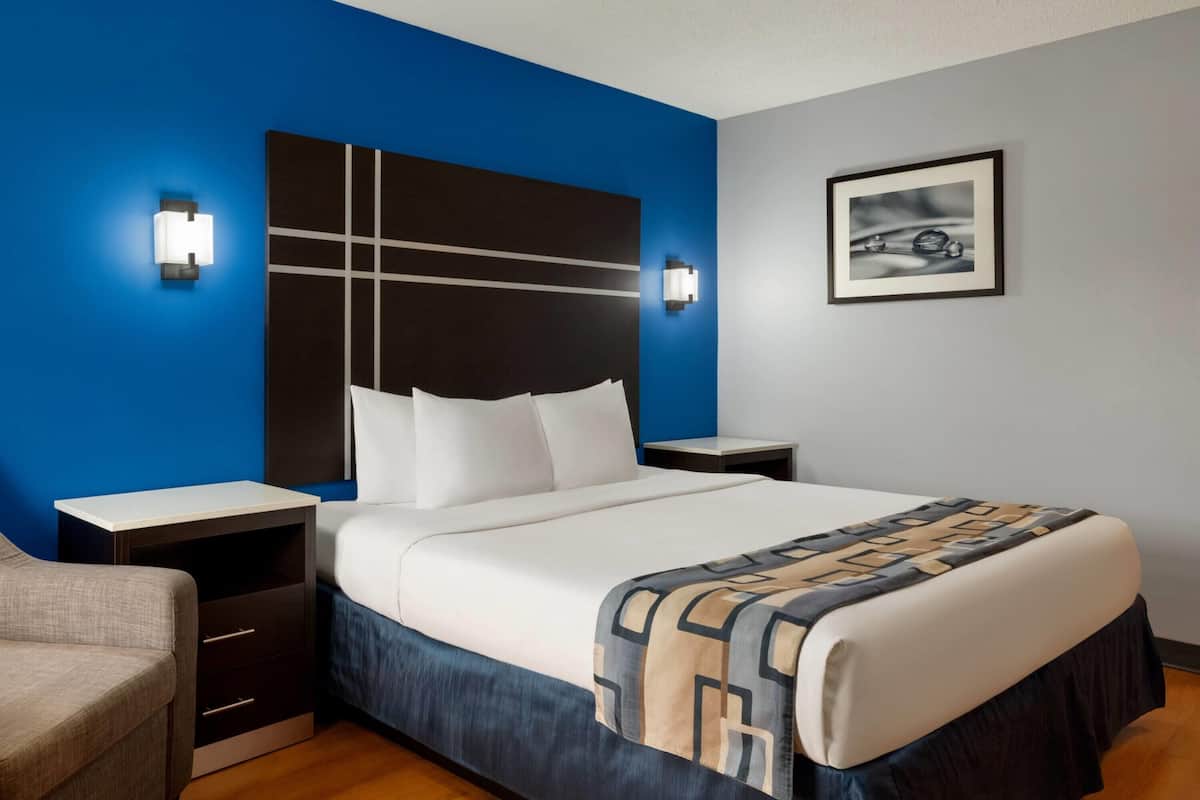 A hotel room with a large bed, two bedside tables, a nightstand, a chair, and a framed picture on the wall.