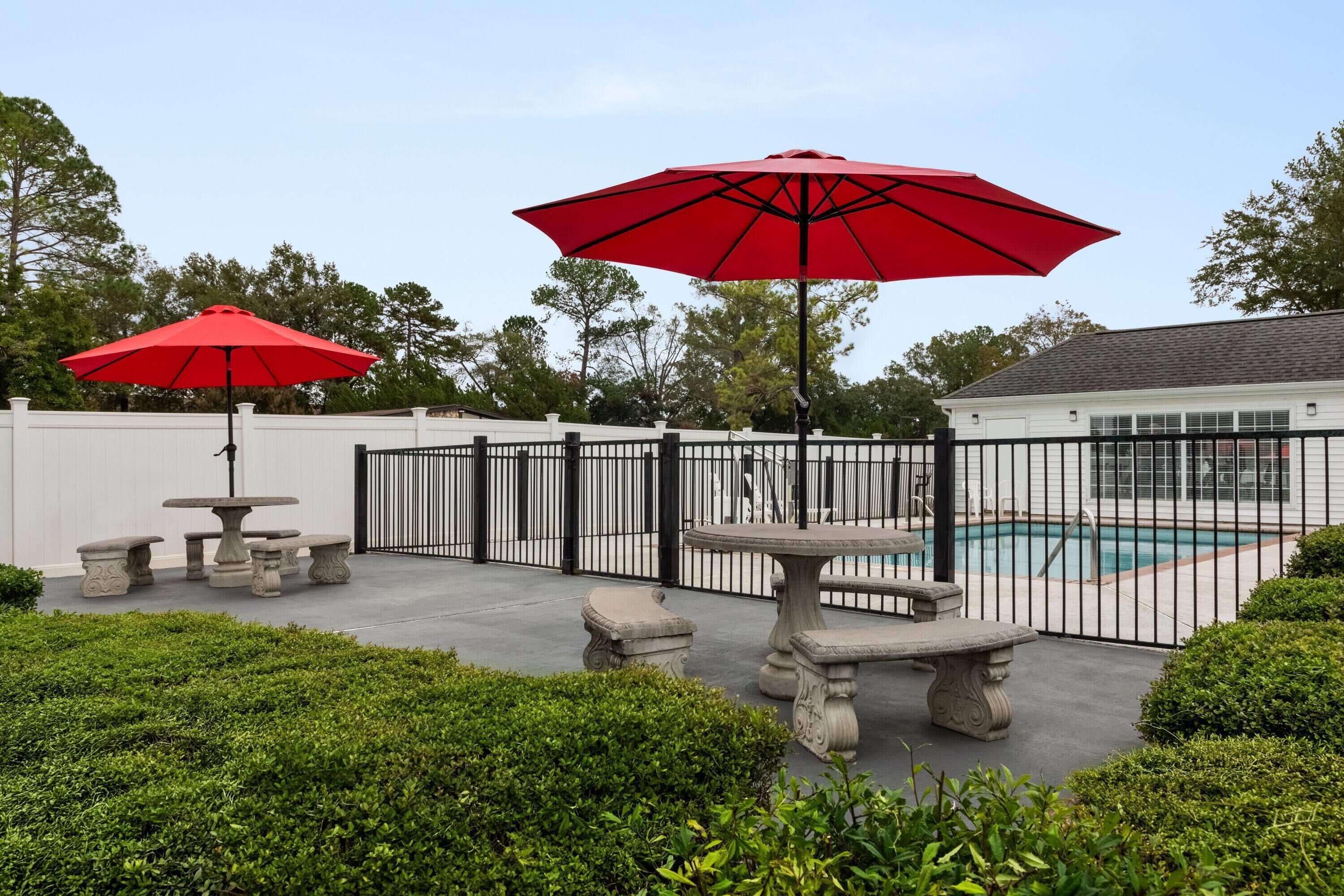 A backyard with a pool, stone tables, and red umbrellas.