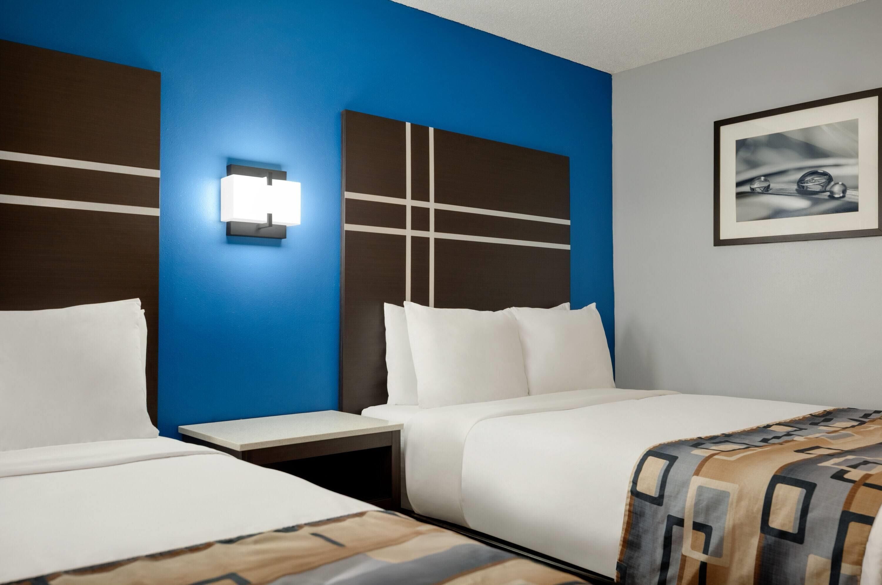 Una habitación de hotel con dos camas, una pared de acento azul, una lámpara moderna e imagen enmarcada en la pared.