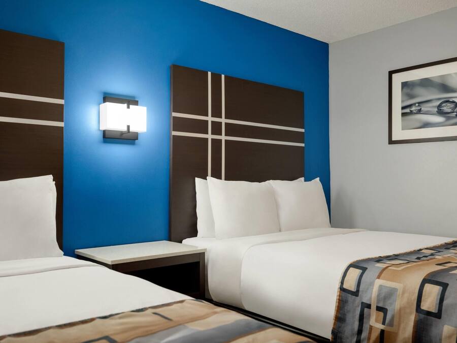 A hotel room with two beds, a blue accent wall, a modern light fixture, and a framed picture on the wall.