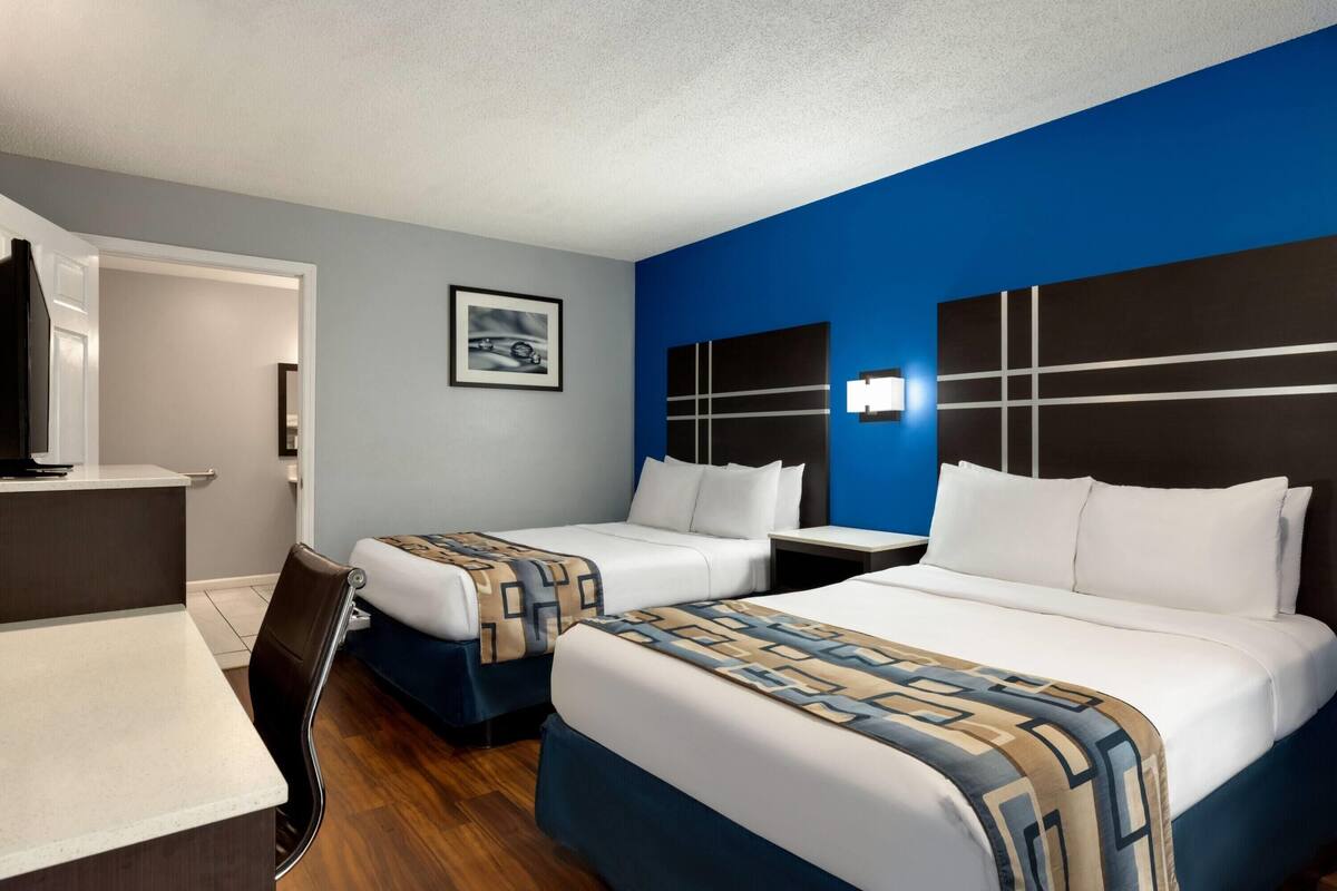 A hotel room with two beds, a desk, a chair, and a TV.