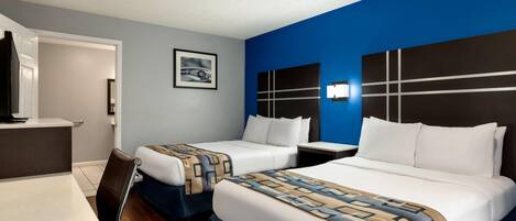 A hotel room with two beds, a desk, a chair, and a TV.