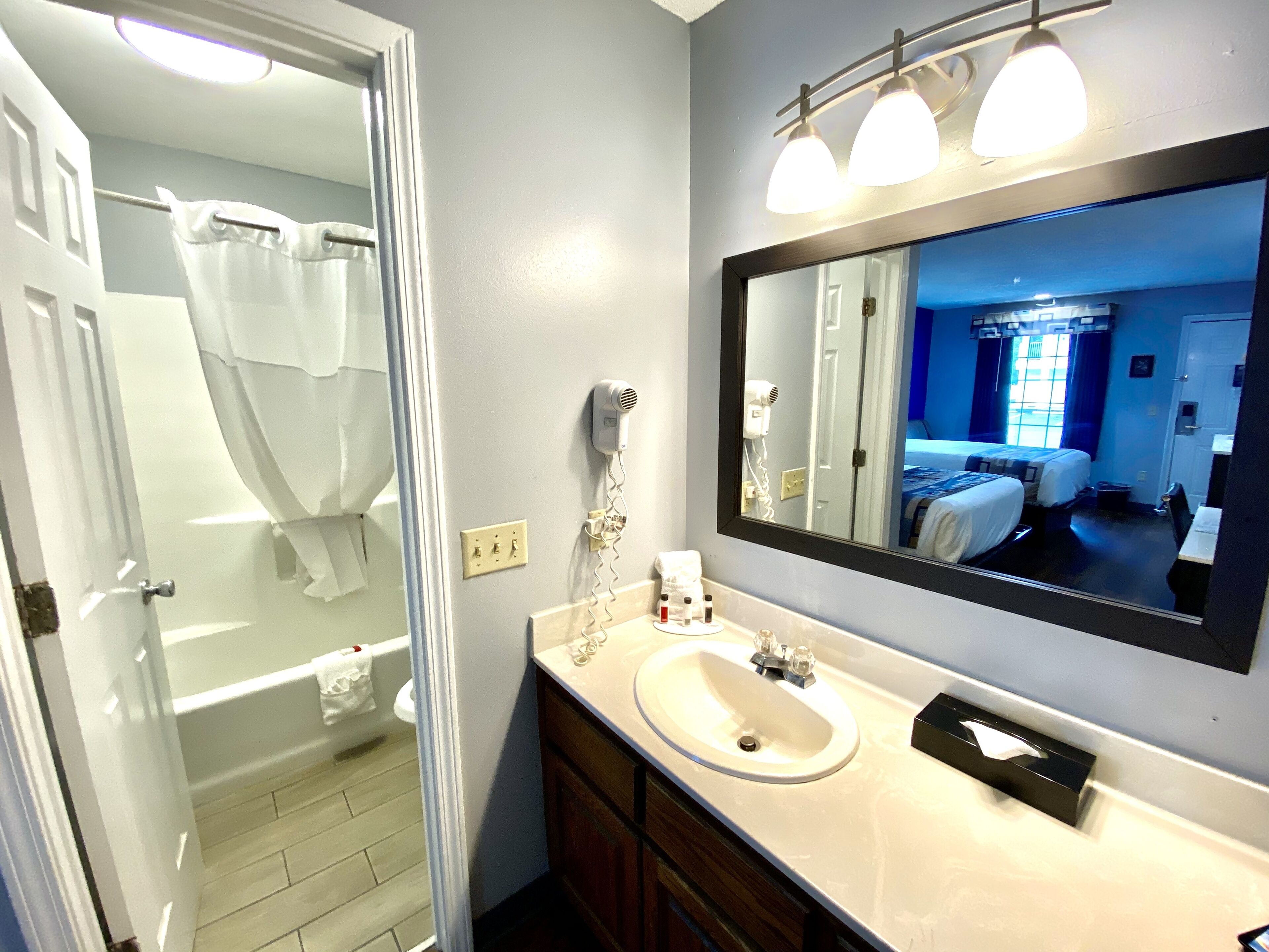 A bathroom with a bathtub, a sink, a mirror, and a hairdryer on the wall.