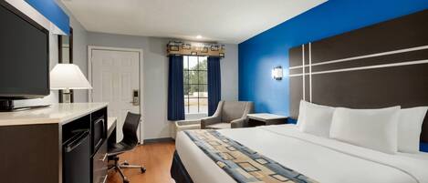 A hotel room with a bed, desk, chair, TV, and a window with curtains.