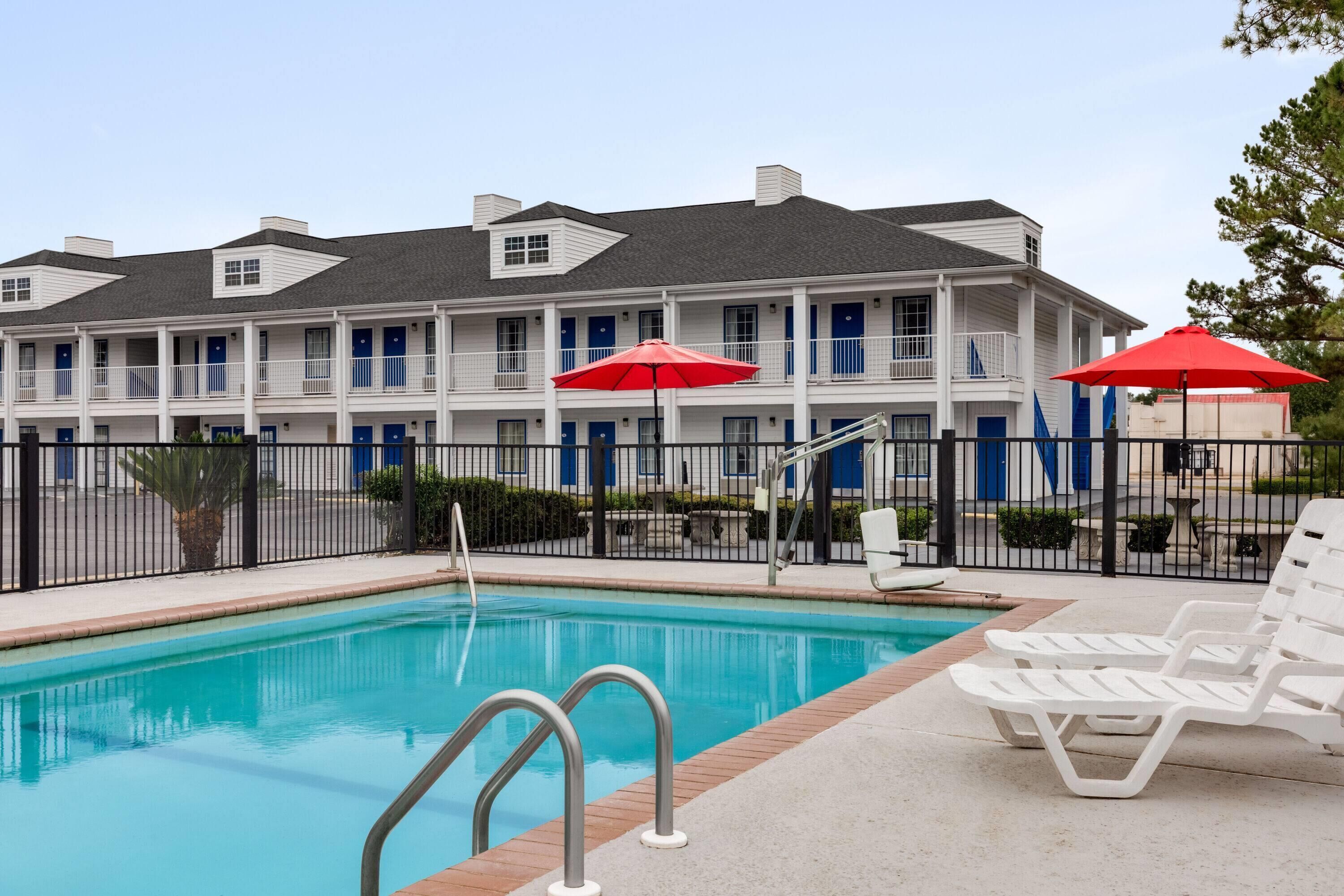 A swimming pool with a metal ladder, white lounge chairs, and red umbrellas.