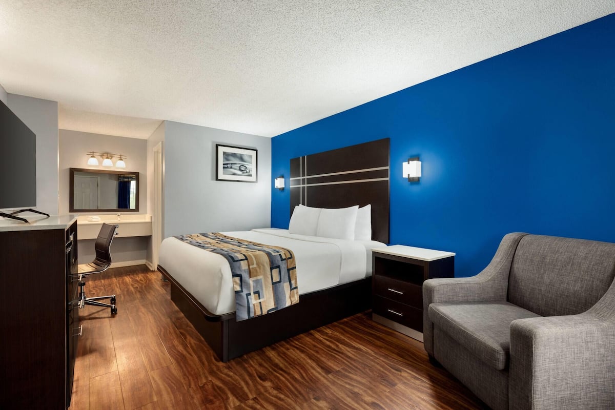 A hotel room with a bed, desk, chair, and a blue accent wall.