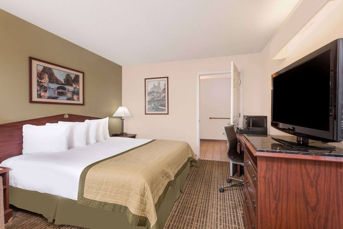 A hotel room with a bed, a desk with a television, and two framed pictures on the wall.