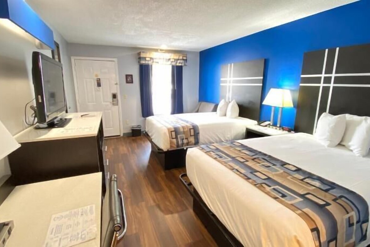 Une chambre d’hôtel avec deux lits, un bureau, une chaise, une télévision et une fenêtre avec des rideaux.