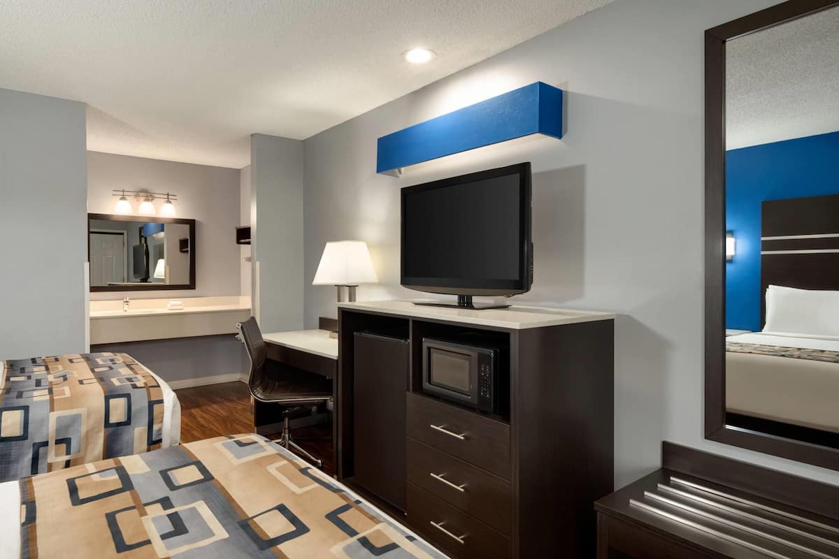 A hotel room with a bed, a desk with a computer, a TV, a microwave, and a mirror.