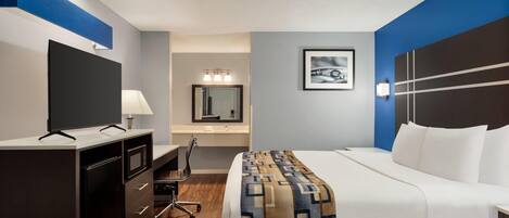 Una habitación de hotel con cama, escritorio con computadora, televisión, espejo y baño.