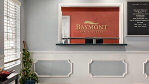 A reception area with a Baymont Inn & Suites sign, a potted plant, and a wall-mounted information board. - Baymont by Wyndham Albany at Albany Mall (Albany)