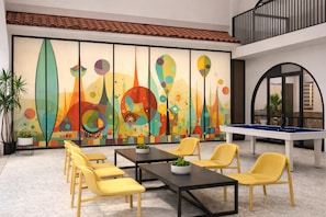 Un espace de loisirs comprenant une table de billard, des chaises jaunes et une fresque murale abstraite aux couleurs vives.